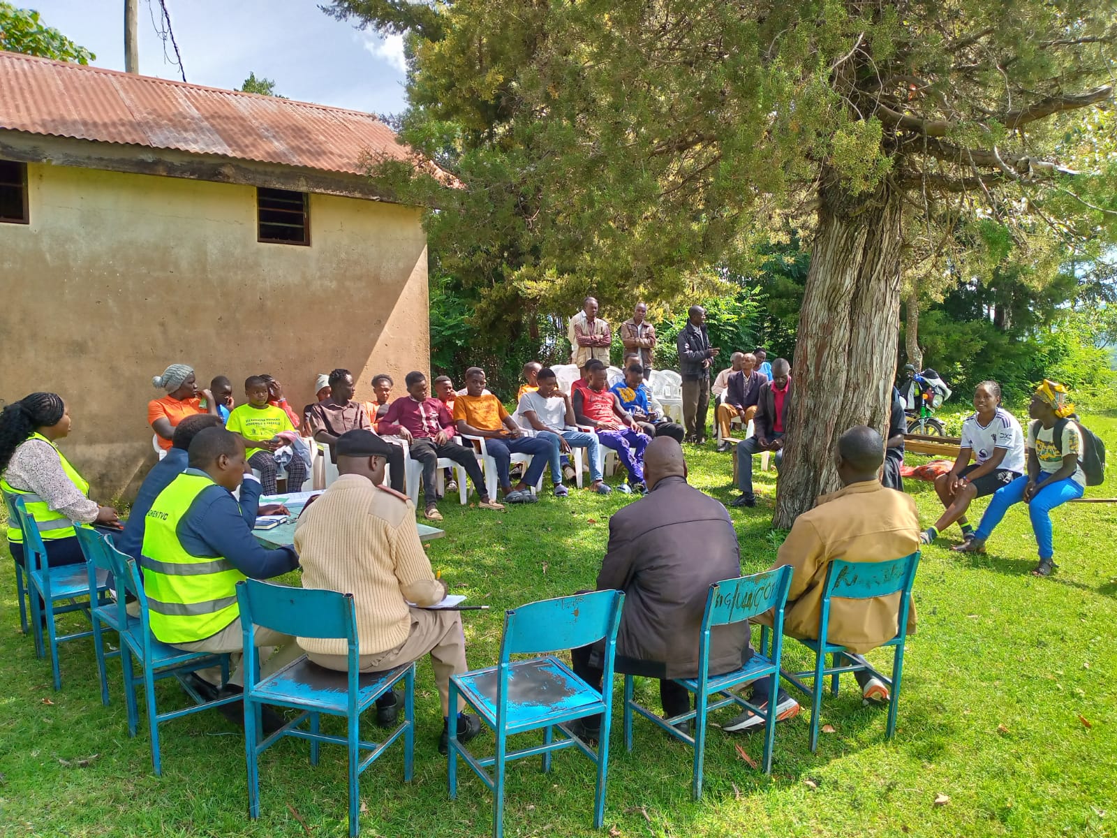 Participants seated in a circular outdoor discussion setup at Emgwen TVC with facilitators and students engaging.