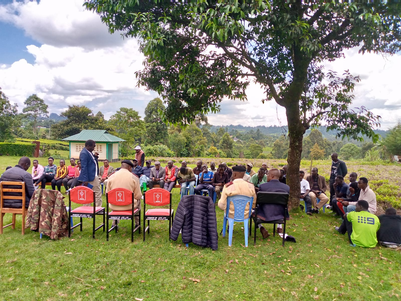 Wide view of students and facilitators seated outdoors on the grass during an Emgwen TVC outreach forum.